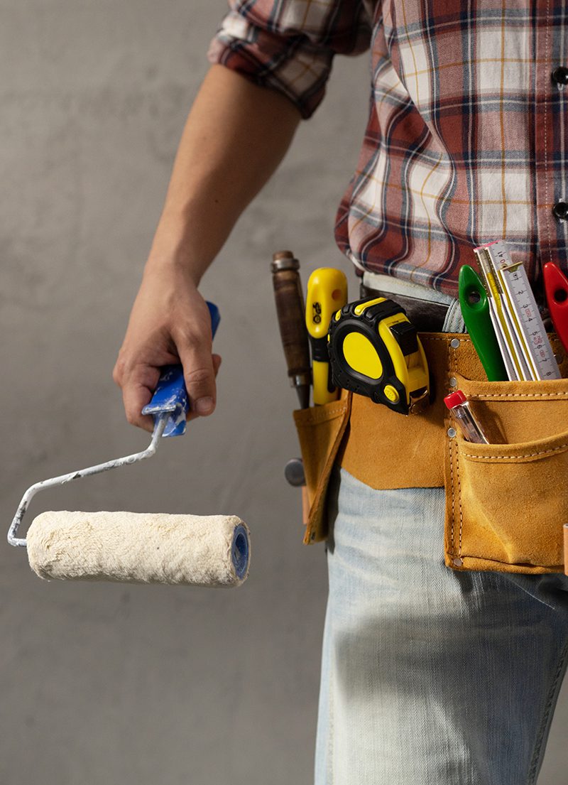 Construction worker man holding paint roller tool near concrete or plaster wall. Male hand and construction tools for house room renovation. Home renovation concept