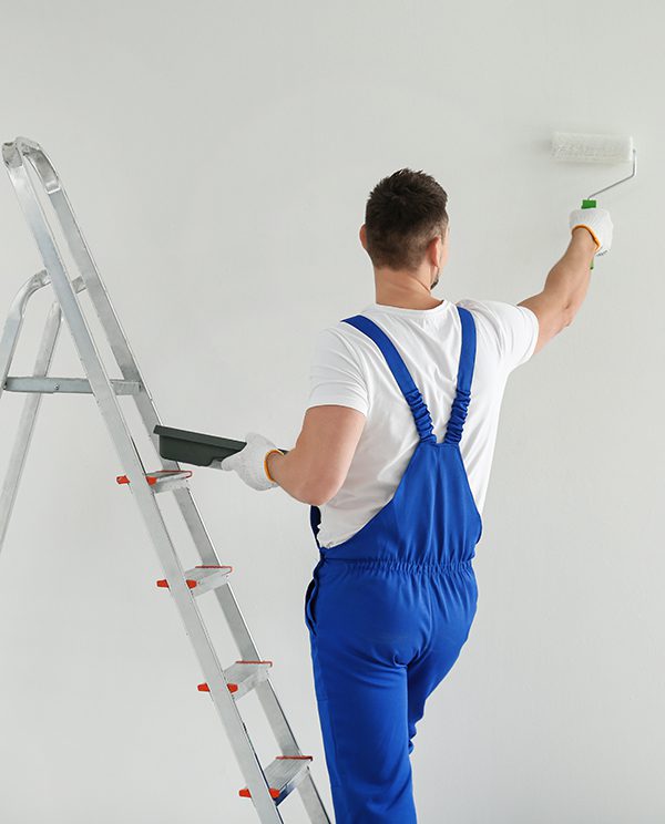 Man painting wall with white dye indoors, back view